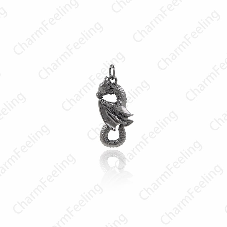 May include: A silver dragon charm pendant with detailed wings and a curled tail. The dragon is facing to the left and has a textured surface.