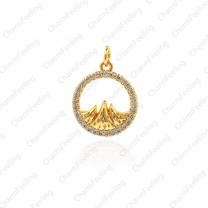 May include: A gold pendant charm featuring a mountain range silhouette inside a circle of clear cubic zirconia stones.