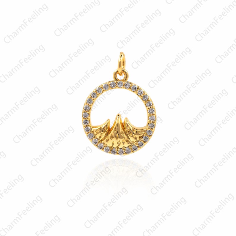 May include: A gold pendant charm featuring a mountain range silhouette inside a circle of clear cubic zirconia stones.