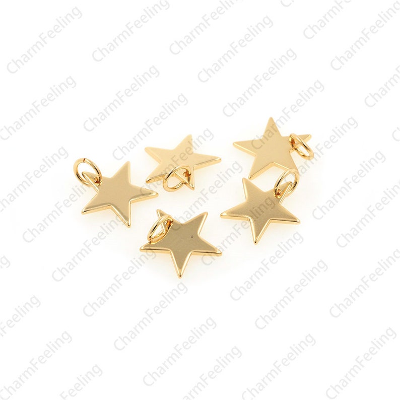 May include: Five gold-coloured star-shaped charms with jump rings. The charms are scattered on a white background.
