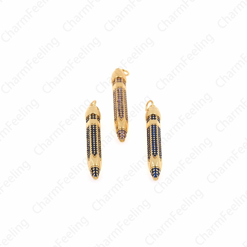 Pu&ograve; includere: Tre ciondoli a forma di matita dorati con strass blu e trasparenti. I ciondoli sono lunghi circa 5 cm.