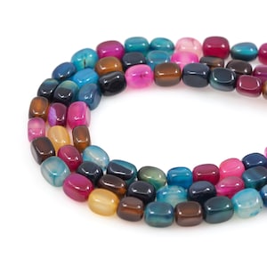 Può includere: Un filo di perline di agata lucida in vari colori, tra cui blu, rosa, marrone e giallo. Le perline sono quadrate con bordi arrotondati. Le perline sono infilate insieme, formando una linea curva su sfondo bianco. Le perline misurano circa 1 cm.