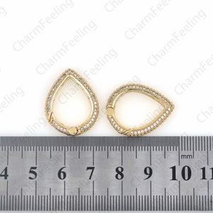 May include: Two gold-tone teardrop-shaped charms with clear crystal accents. The charms are approximately 7 mm in diameter and are shown next to a ruler.