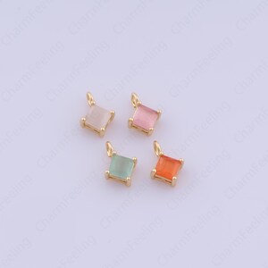 May include: Four small square pendants with gold-colored settings and colorful gemstones. The gemstones are in shades of pink, orange, green, and a light pink. Each pendant has a small loop at the top for attaching to a chain or bracelet.