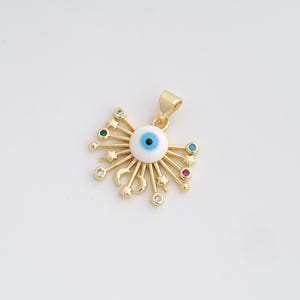 May include: Gold-colored pendant featuring a central white eye with a blue iris, surrounded by radiating lines, stars, and crescent moons. The pendant is adorned with colorful gemstones and has a loop for a chain.
