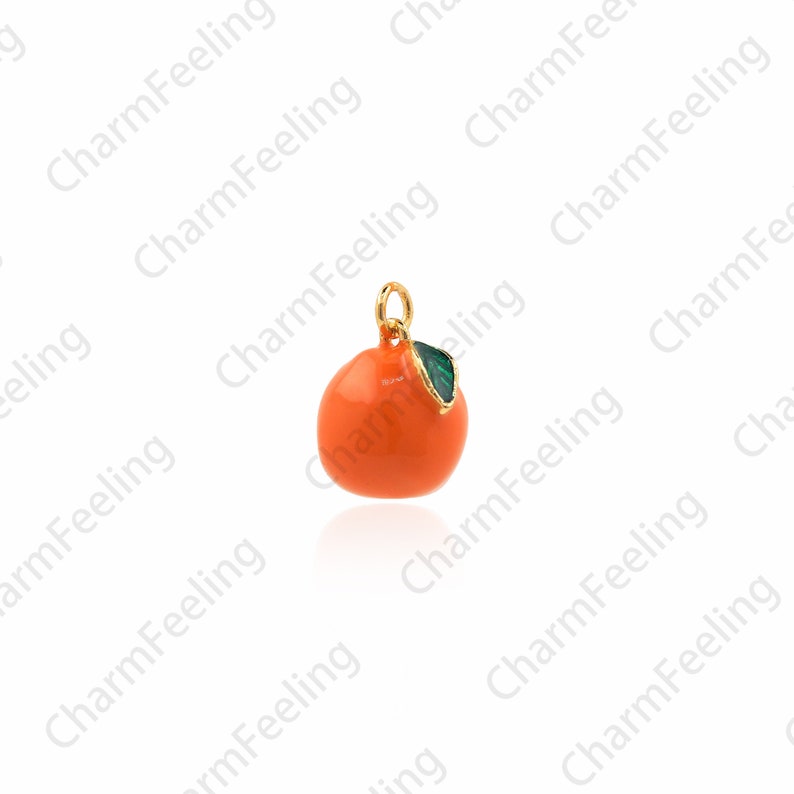 Puede incluir: Un amuleto de oro en forma de naranja con una hoja verde. La naranja es de color naranja brillante y la hoja es de color verde brillante.