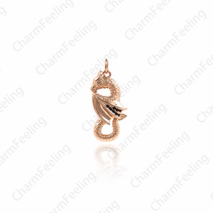 May include: A gold-toned dragon pendant with black accents. The dragon is curled up with its wings spread out. The pendant is on a white background.