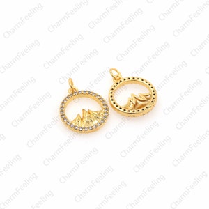 May include: Two gold-tone pendant charms featuring a mountain range design within a circle. The circles are outlined with clear rhinestones.