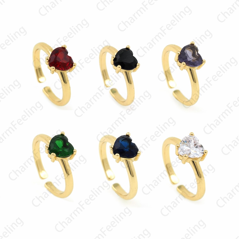 May include: Six gold adjustable rings with heart-shaped gemstones. The rings feature red, black, purple, green, blue, and clear gemstones.