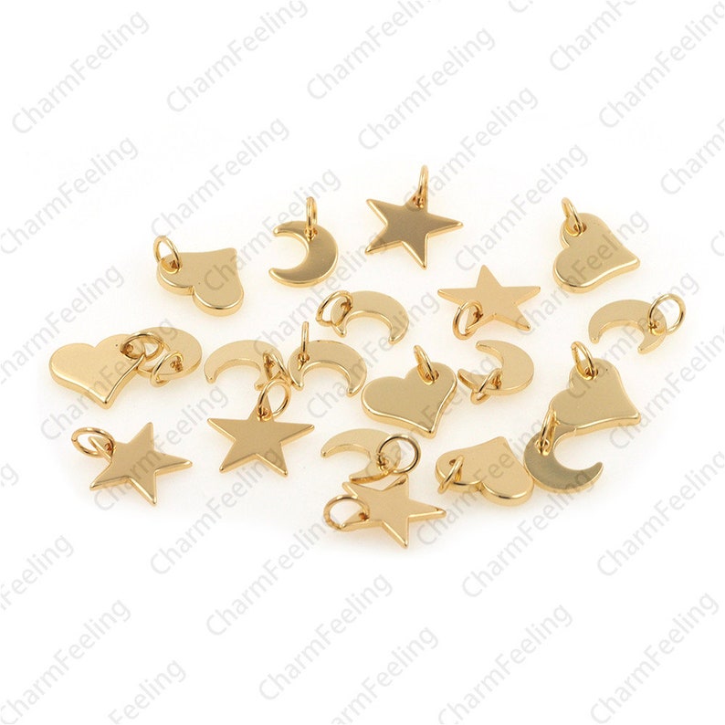May include: A collection of gold-toned metal charms in the shapes of hearts, stars, and crescent moons. The charms have a loop at the top for attaching to jewellery or other crafts.