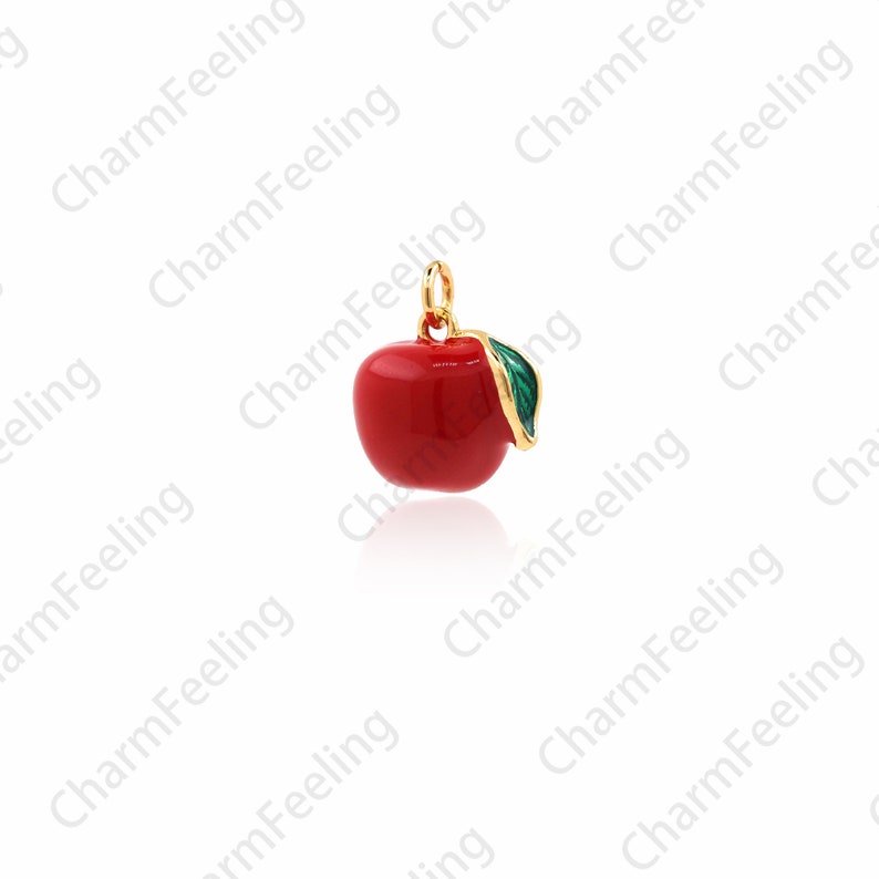 Puede incluir: Un amuleto de oro en forma de manzana roja con una hoja verde. La manzana es un s&iacute;mbolo popular del conocimiento y la educaci&oacute;n.