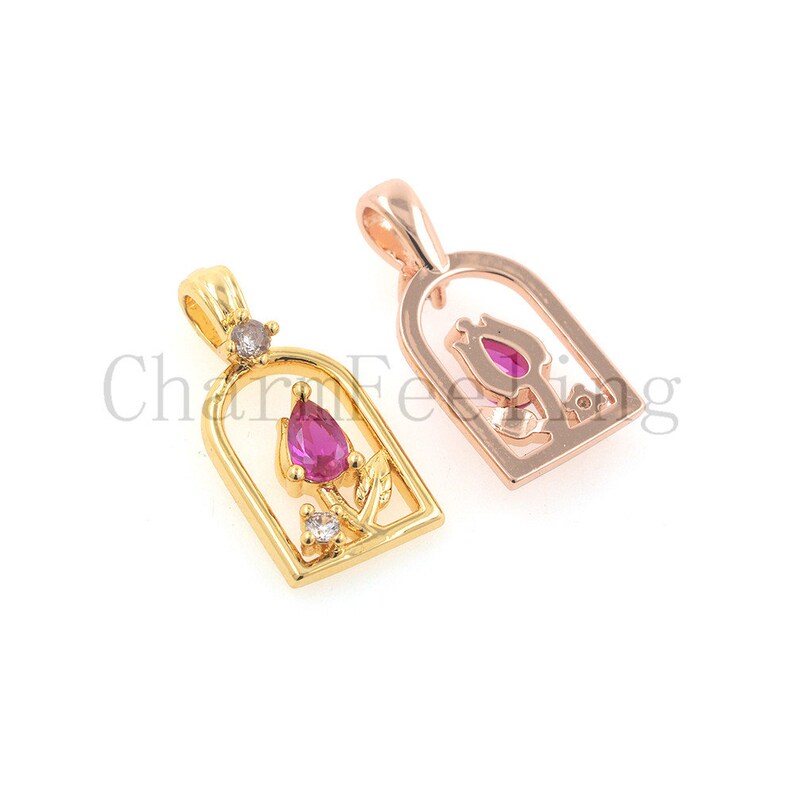 May include: Two gold-tone pendants featuring a rose design. One pendant is rose gold and the other is yellow gold. Both pendants have a pink gemstone in the centre of the rose.