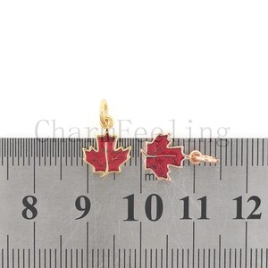 May include: Two gold-colored maple leaf charms with red enamel. The charms are about 1 inch wide and are measured against a ruler.