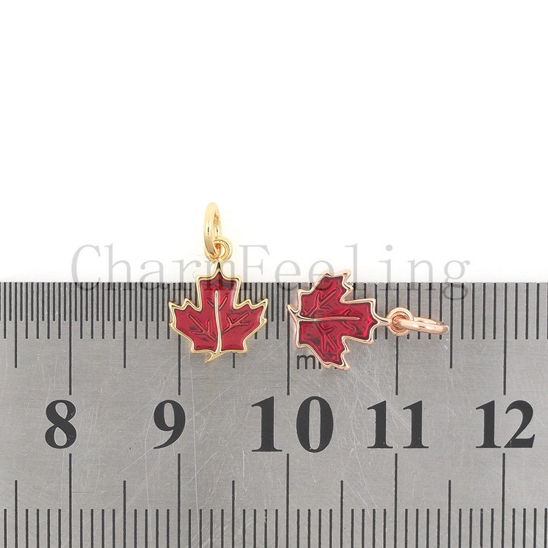 May include: Two gold-colored maple leaf charms with red enamel. The charms are about 1 inch wide and are measured against a ruler.