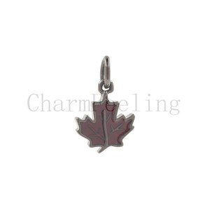 May include: A silver charm in the shape of a red maple leaf. The charm has a loop at the top for attaching to a bracelet or necklace.