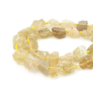 May include: A strand of light brown, raw, natural gemstone beads with a yellow thread connecting them.