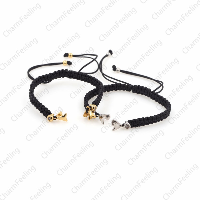 Puede incluir: Dos pulseras trenzadas negras con cierres ajustables. Una pulsera tiene un dije de oro en forma de pez con una peque&ntilde;a piedra transparente. La otra pulsera tiene un dije de plata en forma de coraz&oacute;n con una peque&ntilde;a piedra transparente.