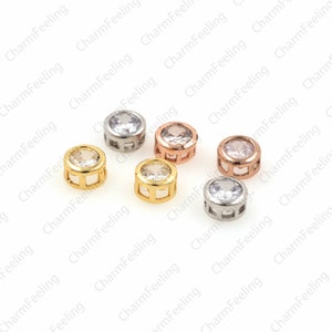May include: Six round metal charms with clear cubic zirconia stones. The charms are in gold, silver, and rose gold.