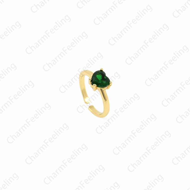 May include: A gold ring featuring a green heart-shaped gemstone. The ring is adjustable and can be worn on any finger.
