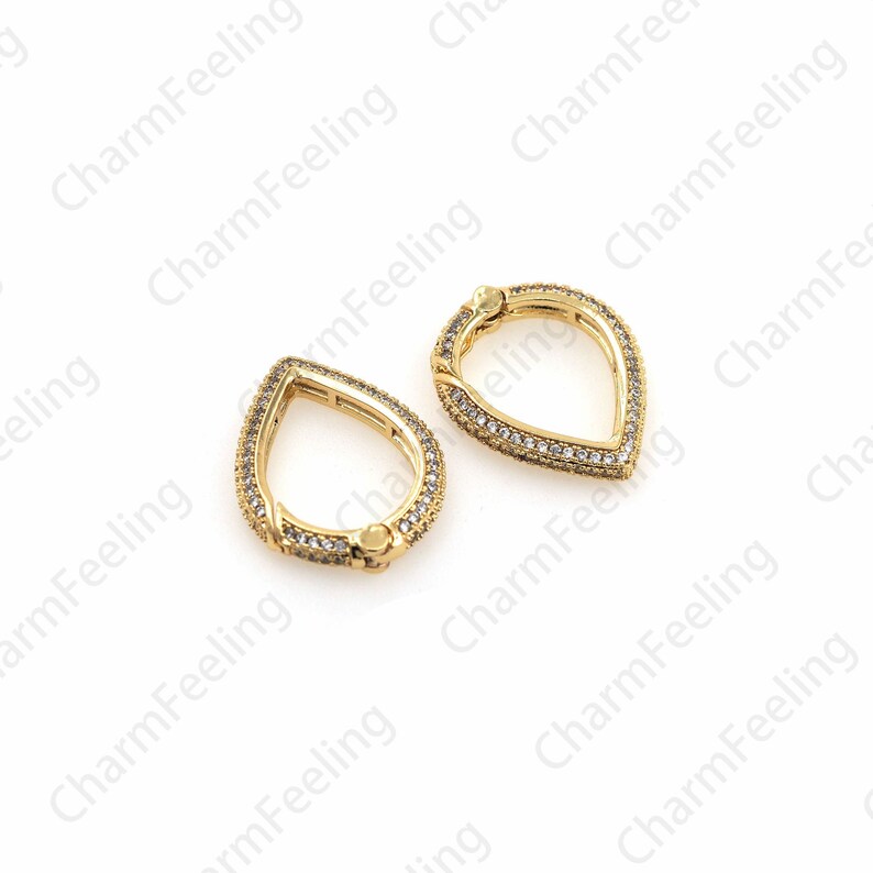 May include: Two gold-tone teardrop-shaped clasps with clear crystal accents. The clasps are open and ready to be attached to a jewelry piece.