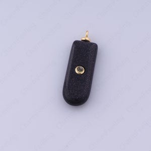 Op de afbeelding: Een donkerblauwe hanger met een goudkleurige beugel en een klein, rond, goudkleurig accent. De hanger heeft een rechthoekige vorm met afgeronde randen en een gespikkelde textuur.