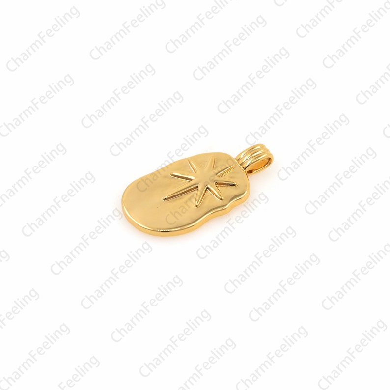 May include: A gold-toned pendant charm featuring a starburst design. The charm is shaped like a rounded rectangle with a slightly irregular edge.