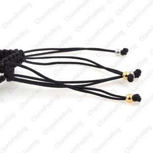 Puede incluir: Primer plano de un cord&oacute;n negro con m&uacute;ltiples hebras y tres cuentas met&aacute;licas. Las cuentas son plateadas y doradas.