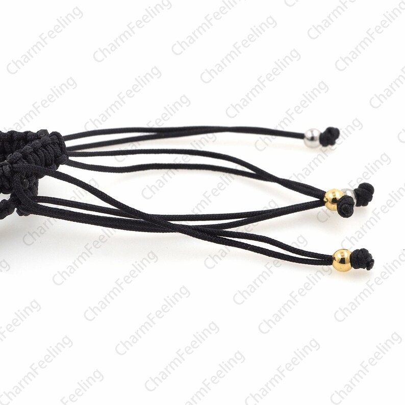Puede incluir: Primer plano de un cord&oacute;n negro con m&uacute;ltiples hebras y tres cuentas met&aacute;licas. Las cuentas son plateadas y doradas.