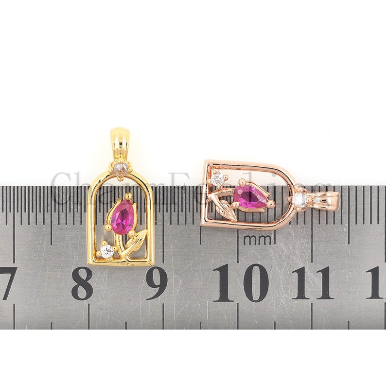 May include: Two gold-tone pendants featuring a pink stone and clear stones in the shape of a flower. The pendants are measured against a ruler with markings in millimetres.