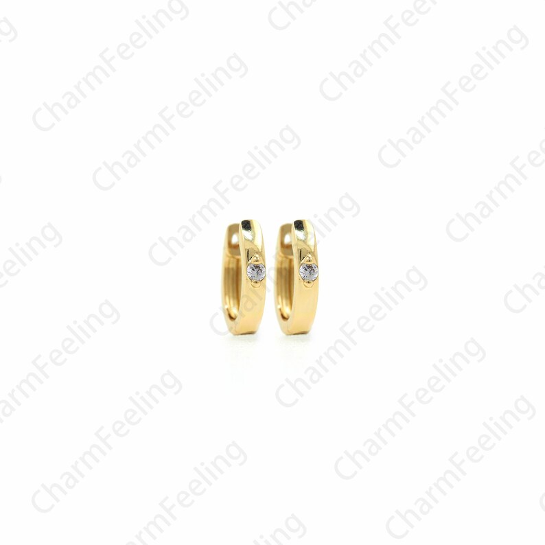 Peut inclure: Une paire de boucles d'oreilles cr&eacute;oles en or avec un petit strass transparent au centre de chaque cr&eacute;ole.