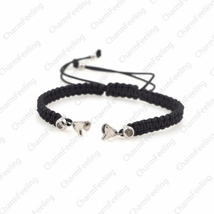 Puede incluir: Un brazalete trenzado negro con dijes plateados en forma de aleta de tibur&oacute;n. El brazalete tiene un cierre de nudo deslizante.