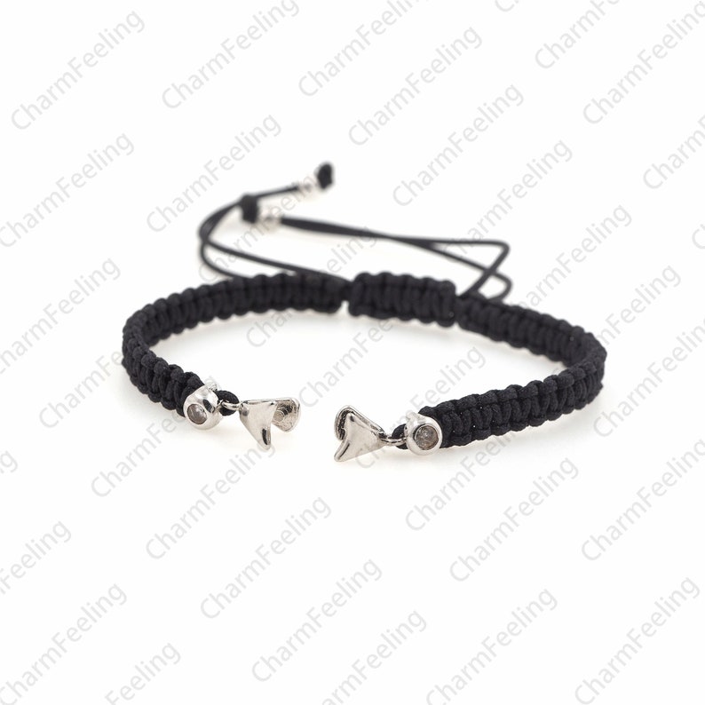 Puede incluir: Un brazalete trenzado negro con dijes plateados en forma de aleta de tibur&oacute;n. El brazalete tiene un cierre de nudo deslizante.