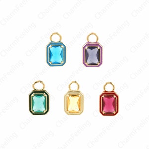 Op de afbeelding: Vijf goudkleurige bedels met verschillende gekleurde glazen stenen. De bedels zijn rechthoekig met afgeronde hoeken en hebben een lus aan de bovenkant om aan een ketting of armband te bevestigen. De stenen zijn blauw, paars, groen, geel en rood.