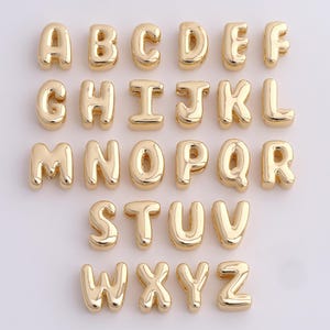May include: A collection of gold-colored alphabet letter charms, each with a rounded, bubble-like design. The letters A through Z are displayed, perfect for personalized jewelry or craft projects.