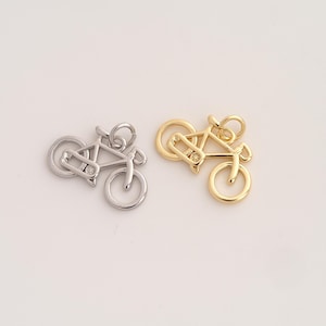 May include: Two bicycle charms, one in a silver tone and one in a gold tone. Each charm features a minimalist outline of a bicycle frame with two circular wheels and a small jump ring attached to the top for hanging as a jewelry component.