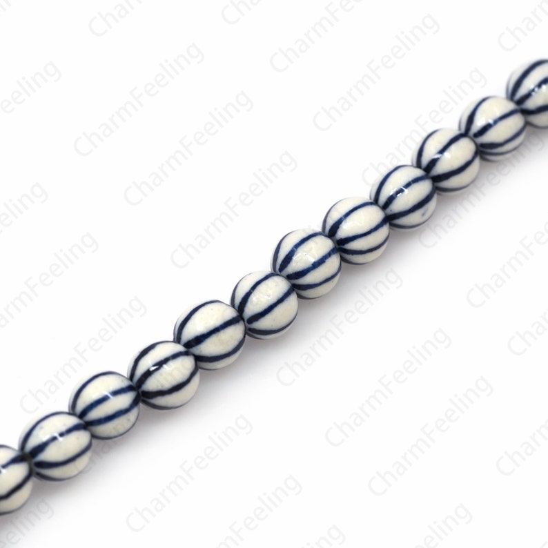 May include: A strand of white ceramic beads with blue stripes. The beads are round and have a glossy finish.