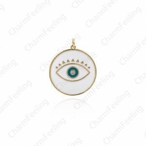 K&ouml;nnte beinhalten: Ein wei&szlig;er Emaille-Anh&auml;nger mit goldener Umrandung und einem blauen b&ouml;sen Auge. Der Anh&auml;nger hat einen kleinen, klaren Stein in der Mitte des Auges.