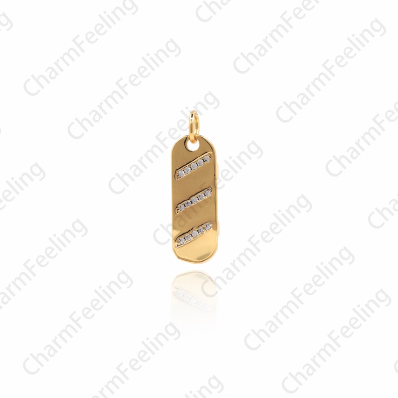 Op de afbeelding: Een gouden bedel met een rechthoekige vorm en een diagonaal patroon van kleine, heldere stenen.