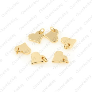 May include: Eight gold-coloured heart-shaped charms with jump rings. The charms are scattered on a white surface.