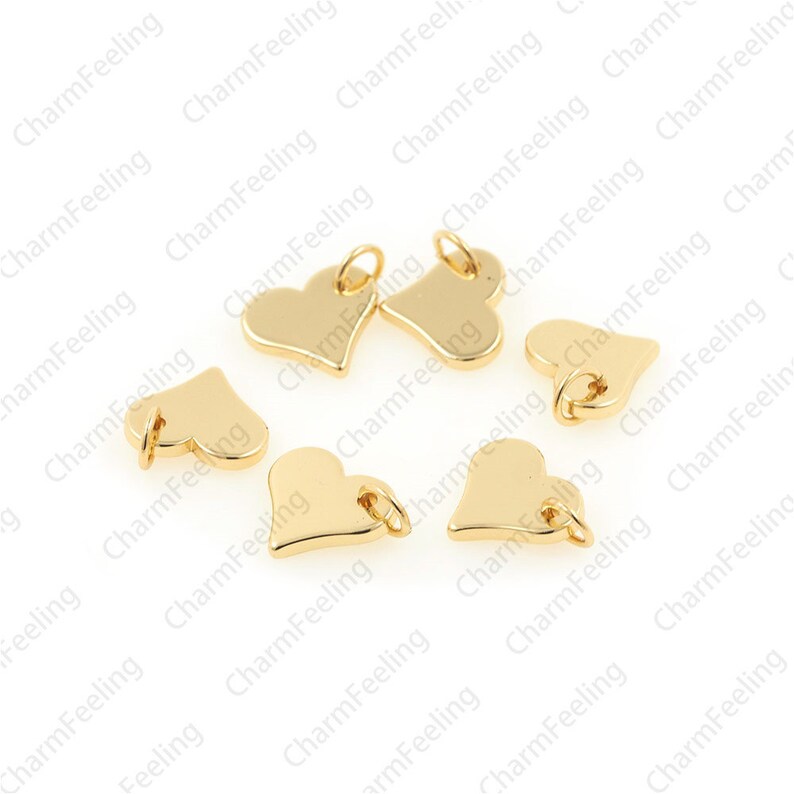 May include: Eight gold-coloured heart-shaped charms with jump rings. The charms are scattered on a white surface.