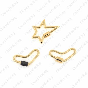 May include: Three gold-toned metal key chain charms. One charm is a star shape, one is a heart shape, and one is a crescent shape. Each charm has a small, black, cylindrical piece in the center.