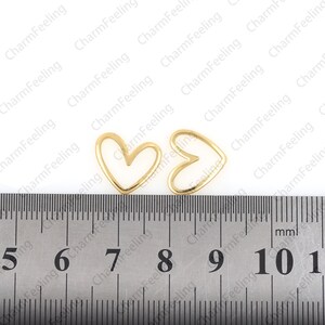 May include: Two gold-colored metal heart-shaped frames, each measuring approximately 1 inch in diameter, are placed on a ruler with markings from 5 to 11.