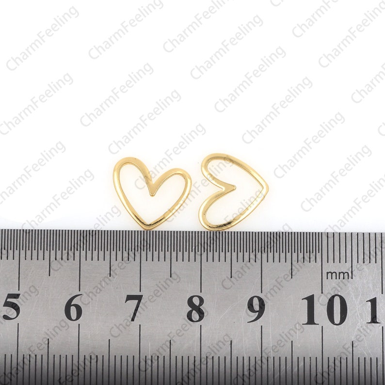 May include: Two gold-colored metal heart-shaped frames, each measuring approximately 1 inch in diameter, are placed on a ruler with markings from 5 to 11.