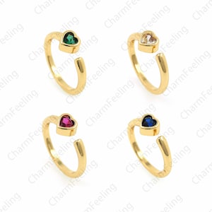 May include: Four gold rings with a heart-shaped stone set in the center. The stones are green, clear, pink, and blue.