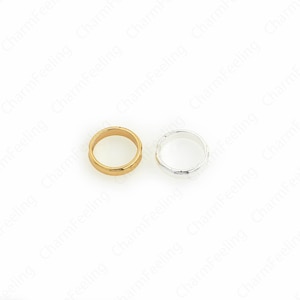 Puede incluir: Dos anillos, uno dorado y otro plateado, se muestran sobre un fondo blanco. El anillo dorado tiene un patrón texturizado alrededor de la banda. El anillo plateado tiene un diseño similar. Ambos anillos son circulares.