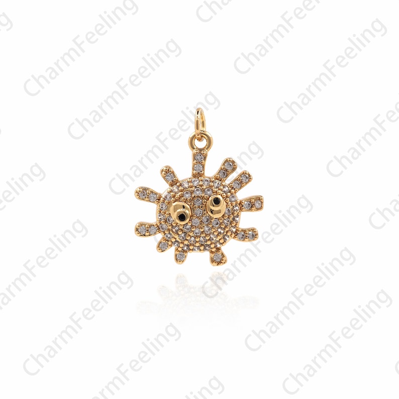 May include: A gold charm in the shape of a cartoon sun with a face. The sun is covered in small, clear rhinestones. The sun has black eyes and a small mouth.