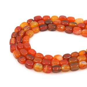 May include: A strand of carnelian beads, each bead is a smooth, oval shape with a reddish-orange color and white streaks.
