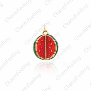 Puede incluir: Un amuleto de color dorado con forma de rodaja de sand&iacute;a. El amuleto es rojo con semillas negras y una c&aacute;scara verde.