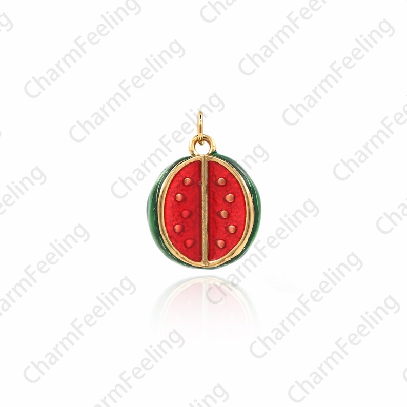 Puede incluir: Un amuleto de color dorado con forma de rodaja de sand&iacute;a. El amuleto es rojo con semillas negras y una c&aacute;scara verde.