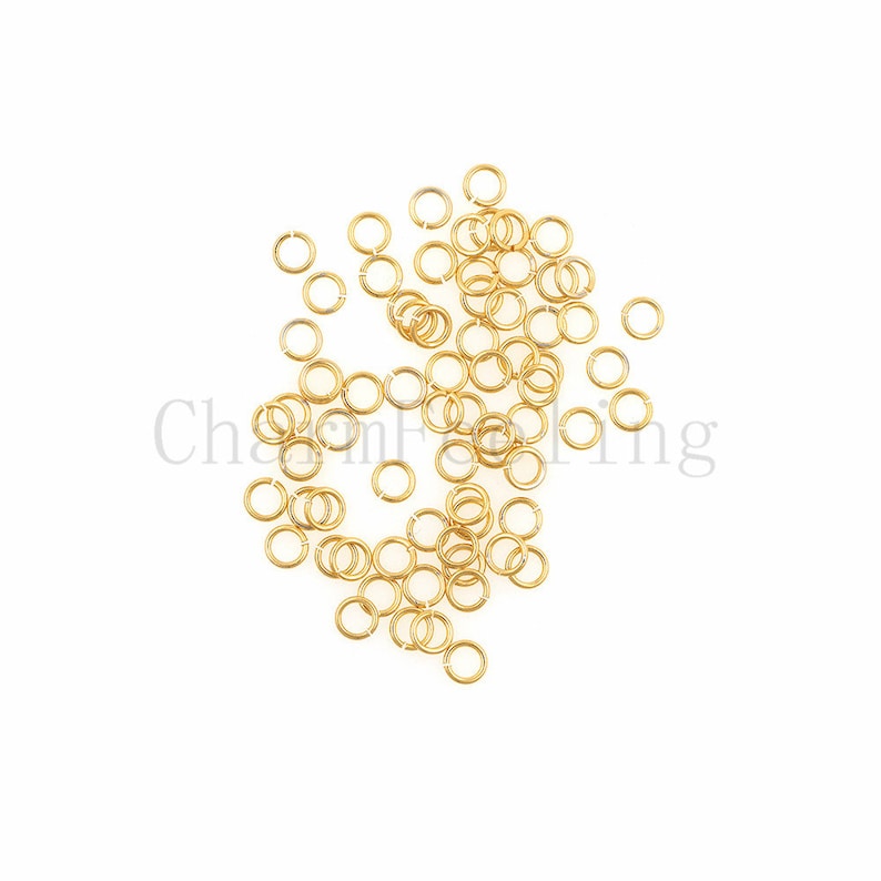 May include: A large quantity of gold jump rings, scattered on a white background. These rings are commonly used in jewelry making.